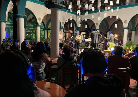 Crowded indoor event in a colonnade-style venue with people in silhouette and blue lighting illuminating the arched architectural space