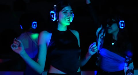 People wearing glowing neon armbands dancing at a dark nightclub with blue and green fluorescent lighting