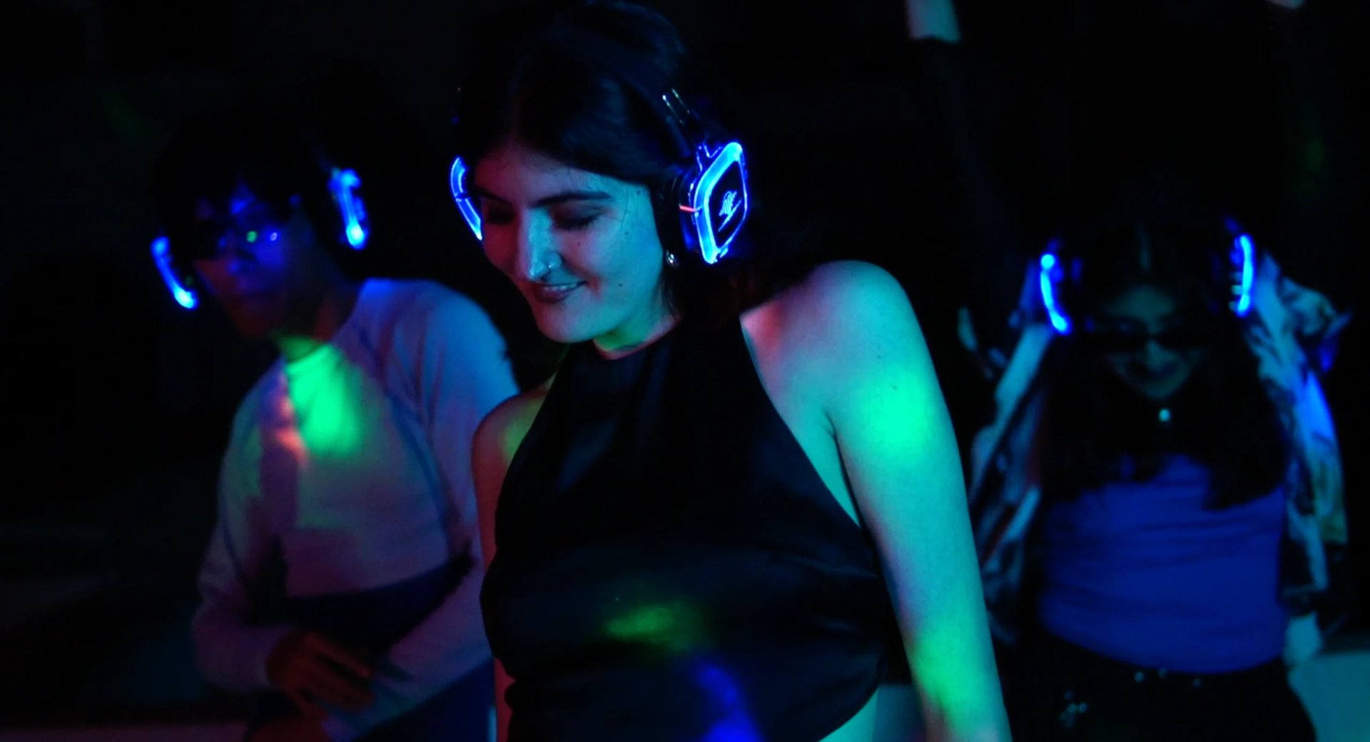 DJ with neon headphones performing at a nightclub with colorful LED lights and dancing crowd